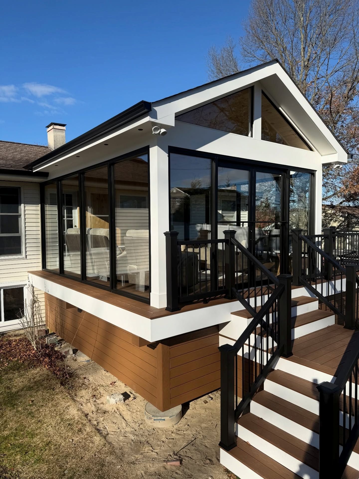 A modern sunroom addition with black-framed windows, white siding, and a wooden deck with black railings and stairs.