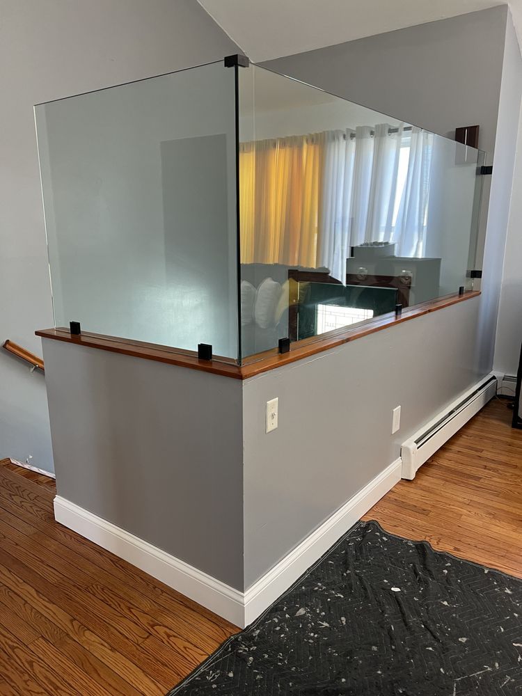 A glass partition installed atop a grey pony wall with wooden trim in a home setting.
