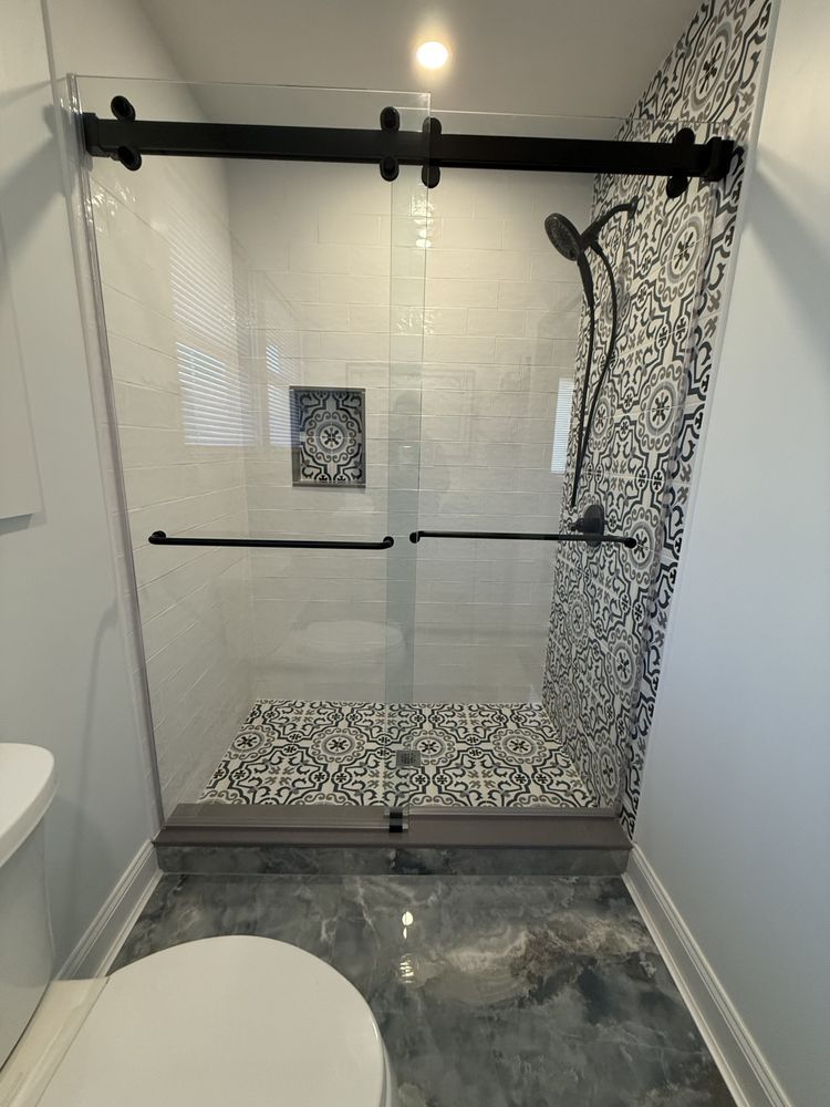 A walk-in shower with a black sliding glass door, patterned tile walls, and matching decorative floor tile.