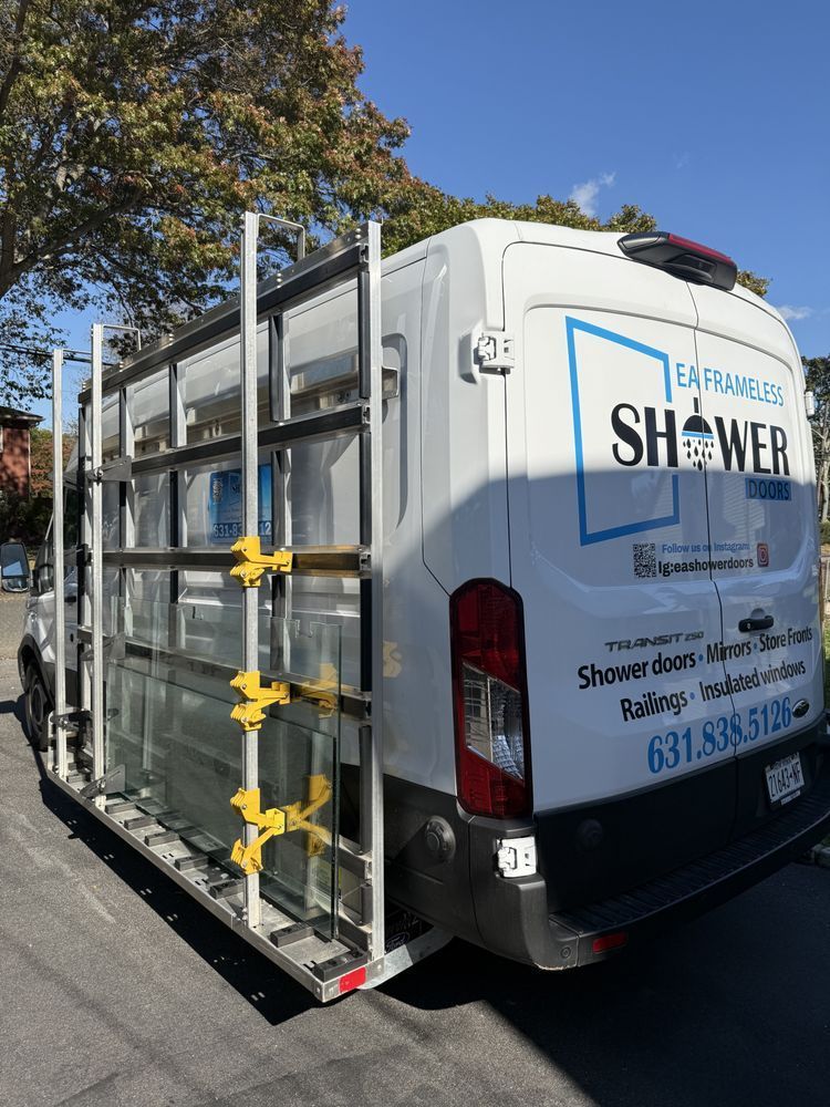 A white van parked outdoors, fitted with a custom exterior rack holding large glass panels for shower door installations.