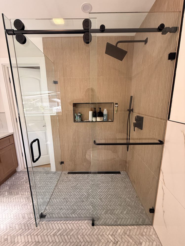 A modern walk-in shower with matte black fixtures, a sliding glass door, tiled walls, and a grey herringbone floor.