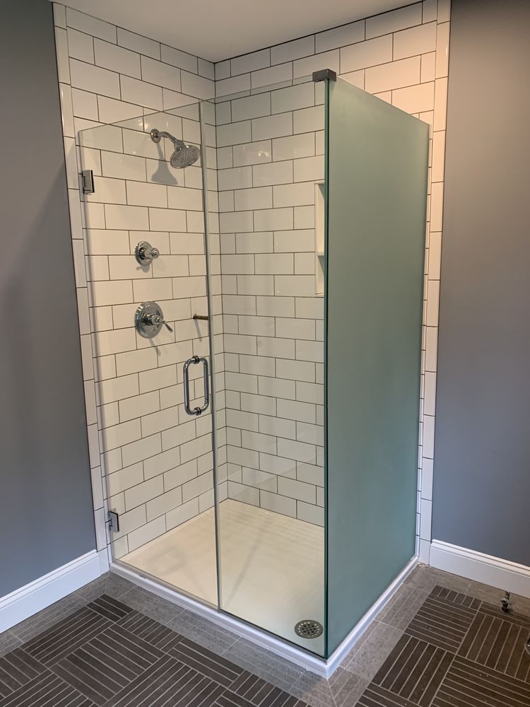 A walk-in corner shower with white subway tile walls, a glass door, and a frosted glass side panel on a tiled floor.
