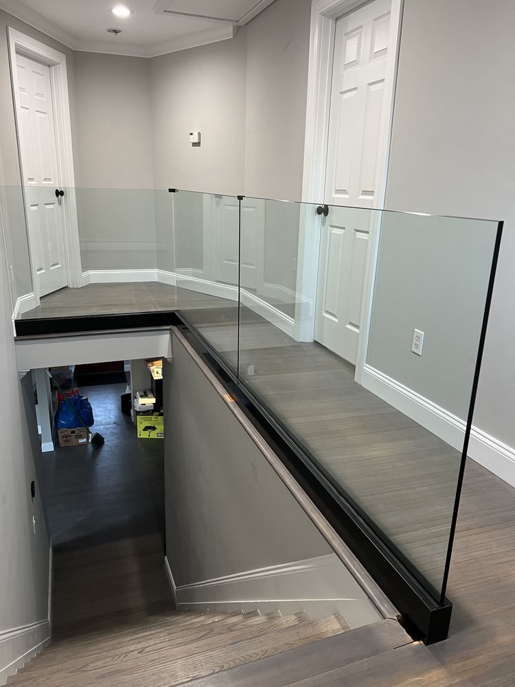 A view looking down a wooden staircase from a landing with a modern frameless glass railing and white interior doors.