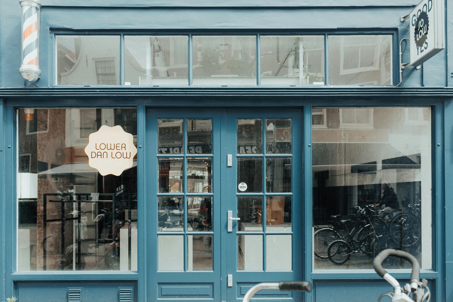 A teal storefront with a glass double door, a barber pole on the left, and a sign in the window.