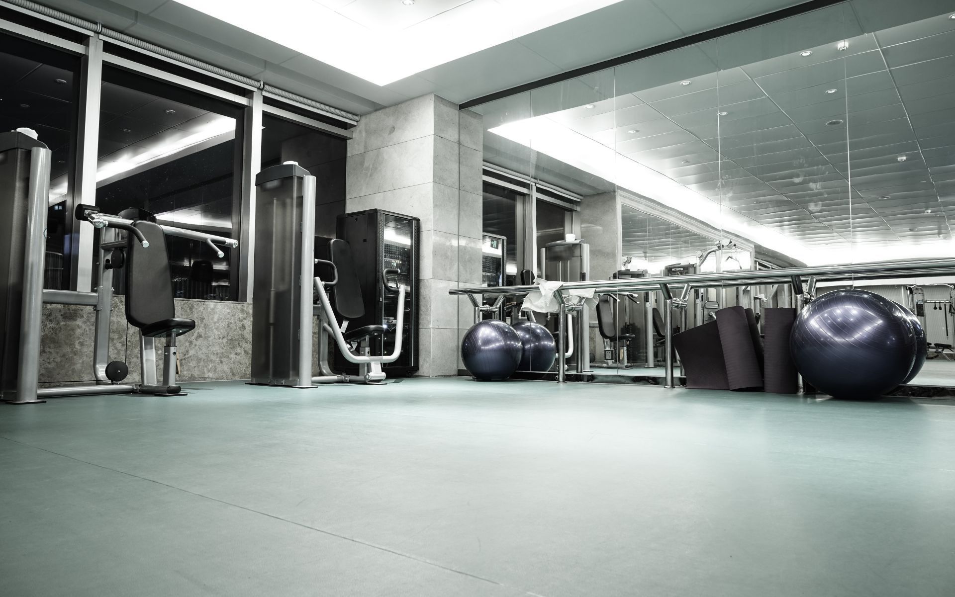 A brightly lit, modern indoor gym featuring various weight training machines, exercise balls, and floor mats.