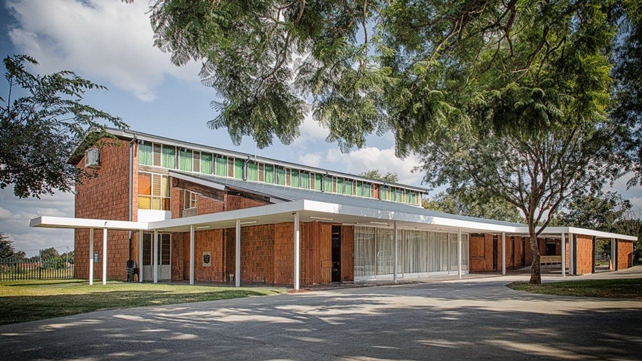 Red brick building with a long white canopy and a green glass windowed roof, under a blue sky.