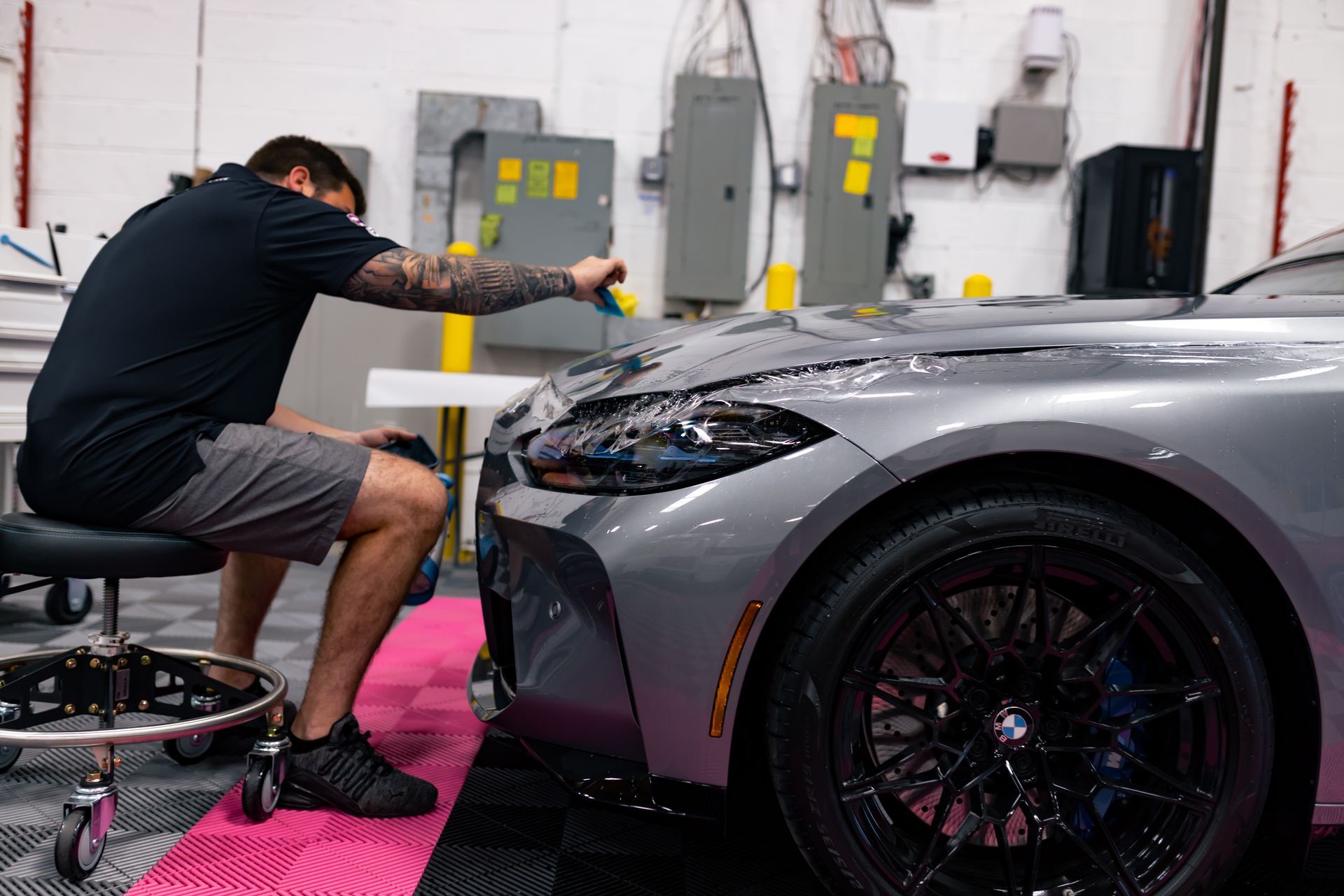 A man is sitting on a stool working on a car in a garage.