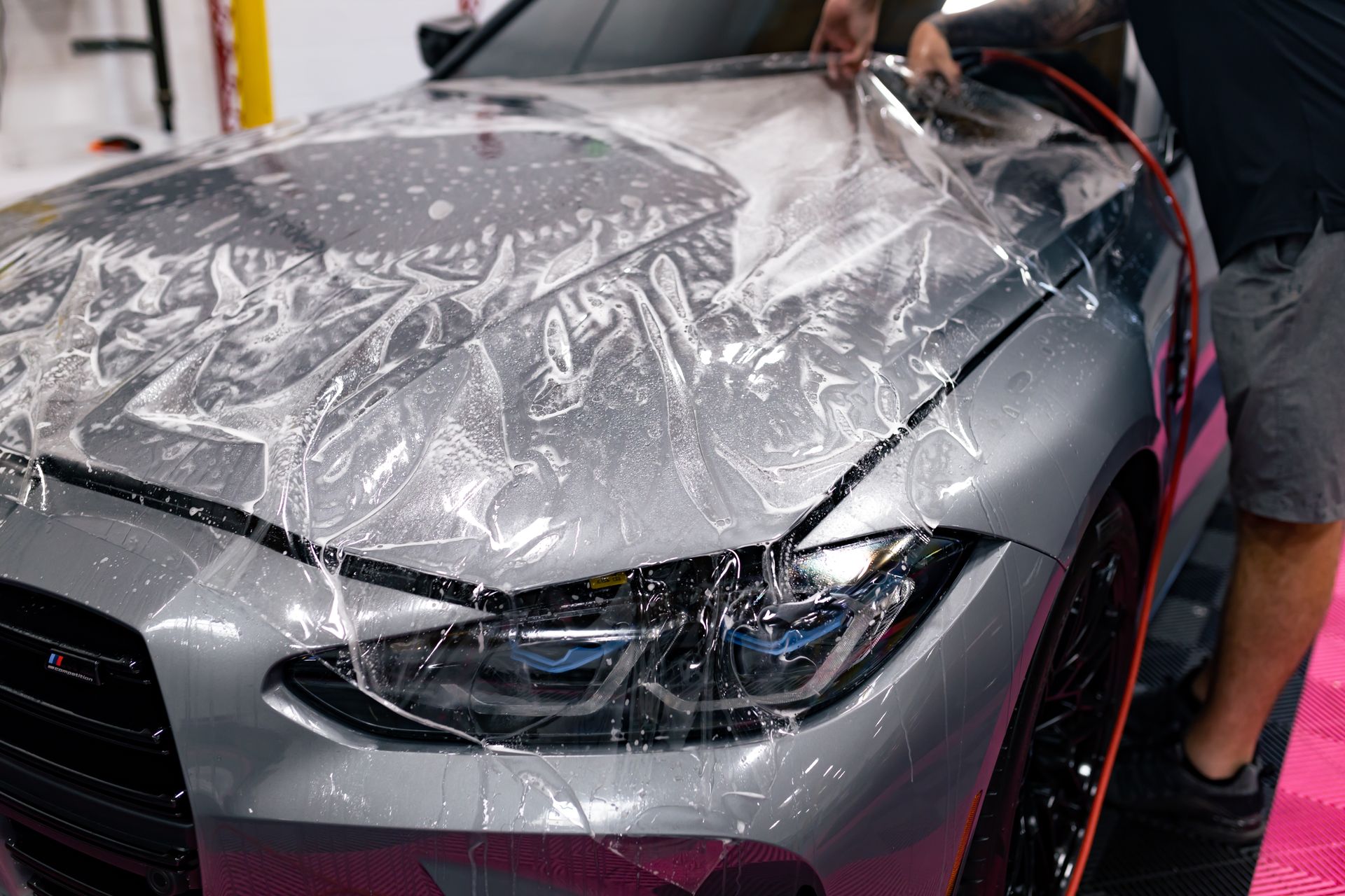 A man is covering the hood of a car with plastic wrap.