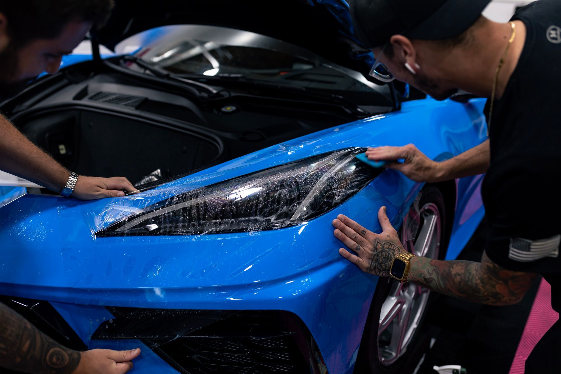 Two men are wrapping a blue car with a protective film.
