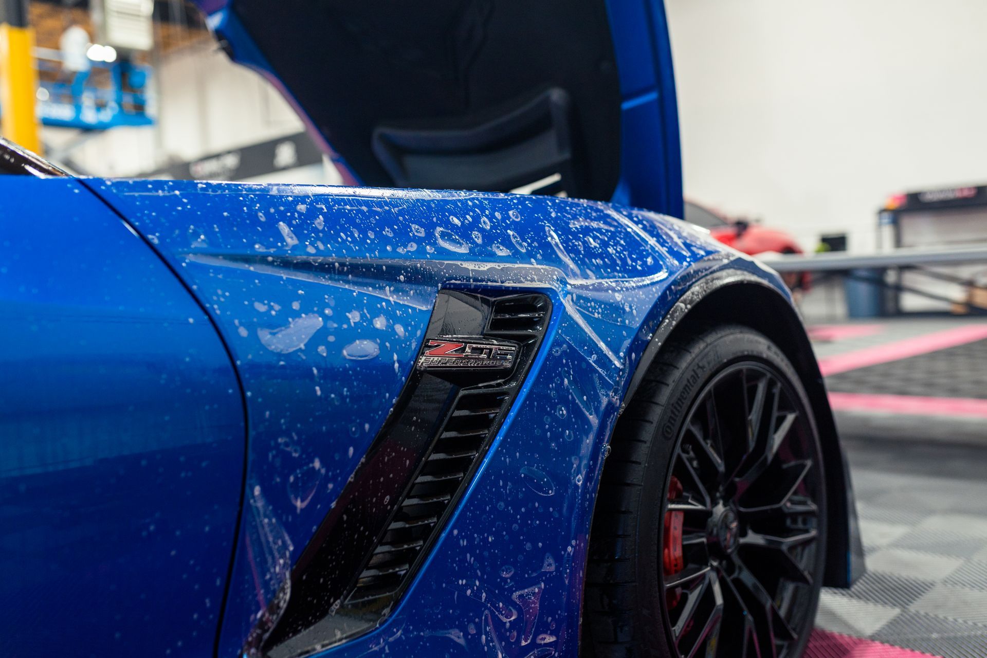 A close up of a blue sports car with its hood open in a garage.