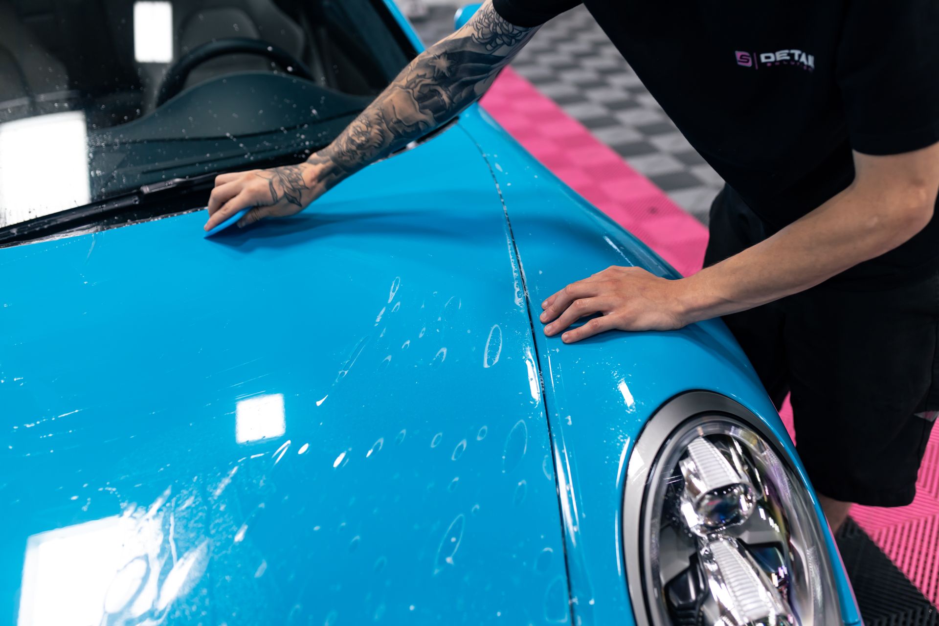 A man is cleaning the hood of a blue car.