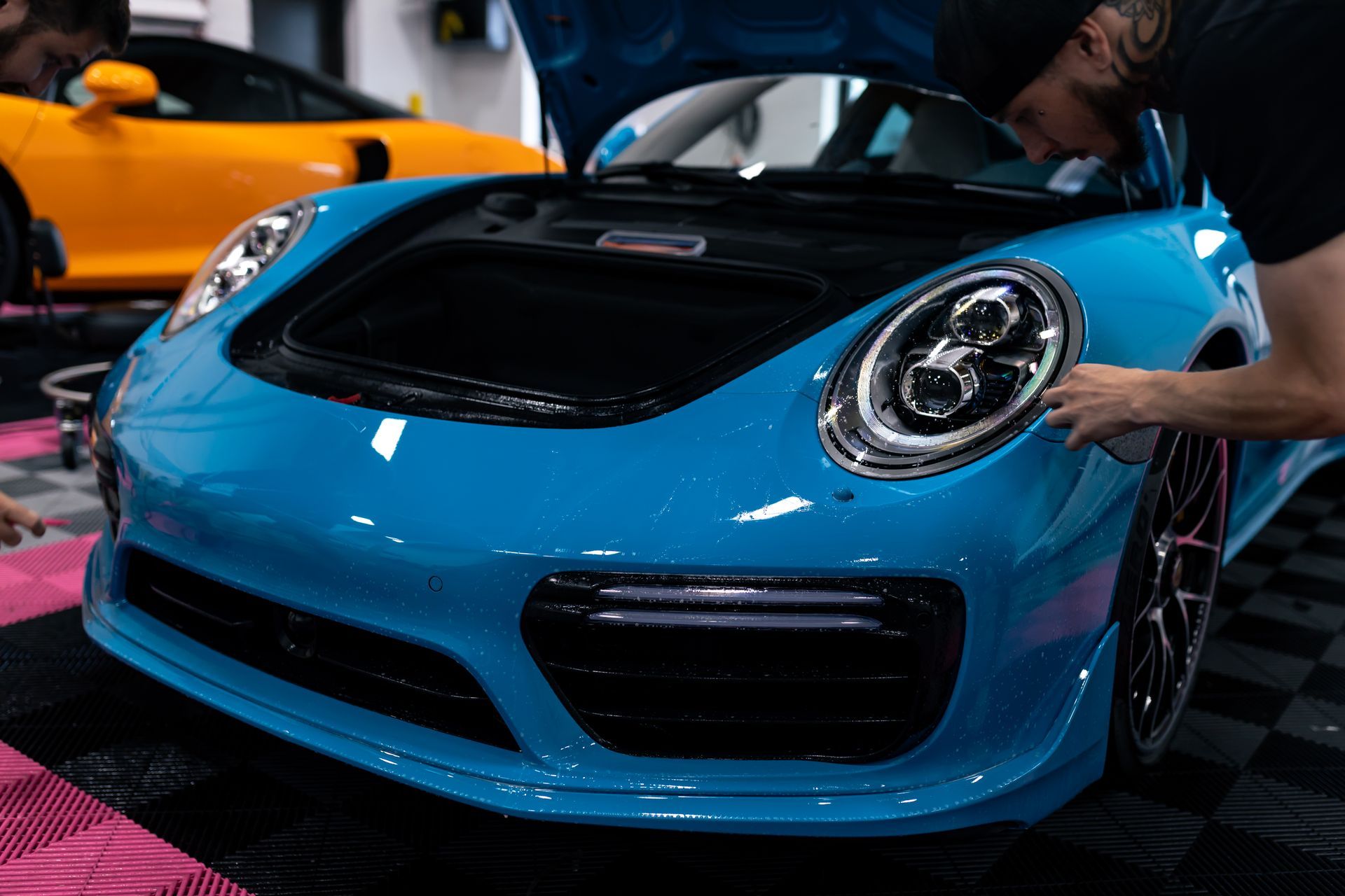 A person is polishing the hood of a blue car.