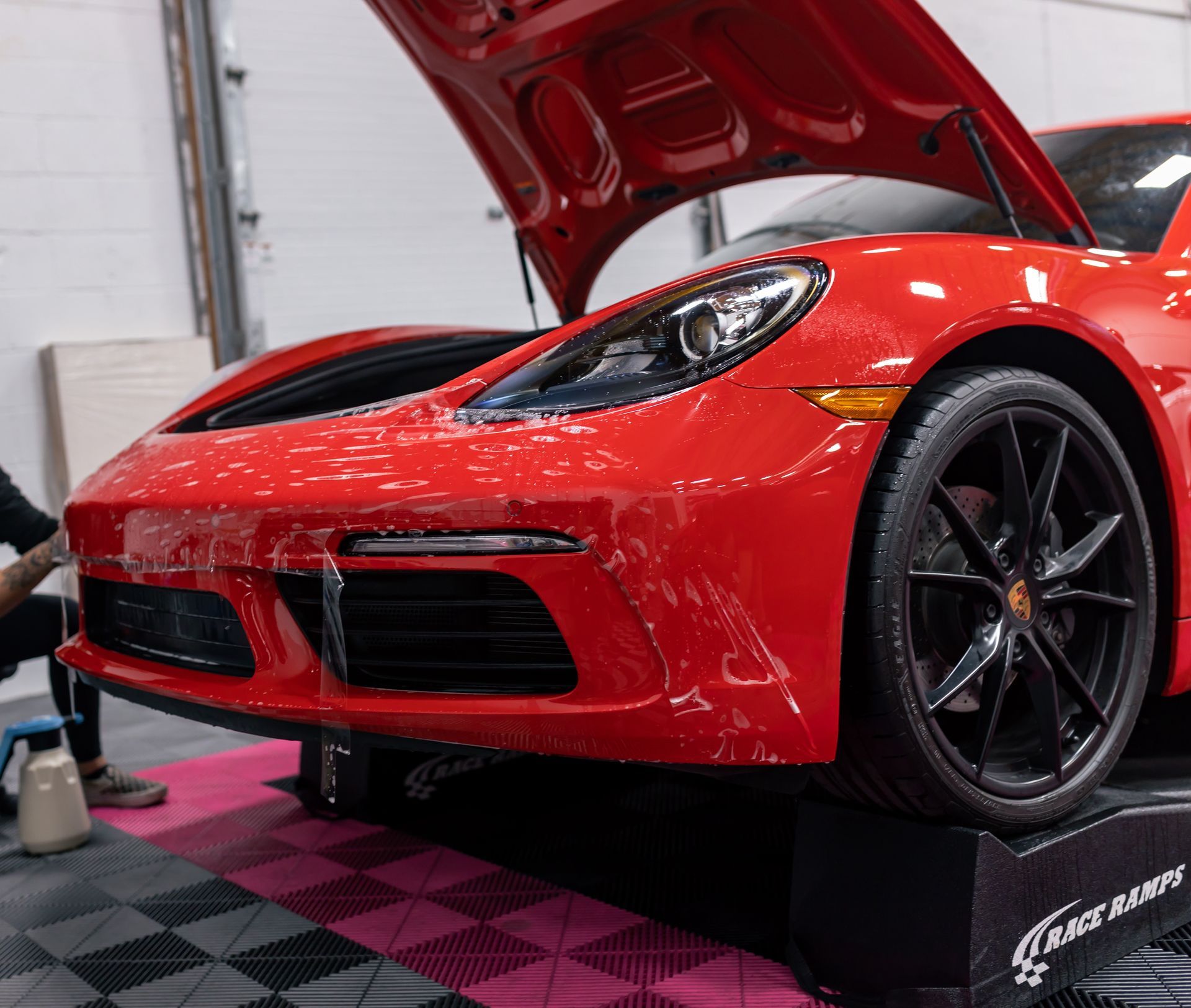 A man is working on a red sports car with the hood up