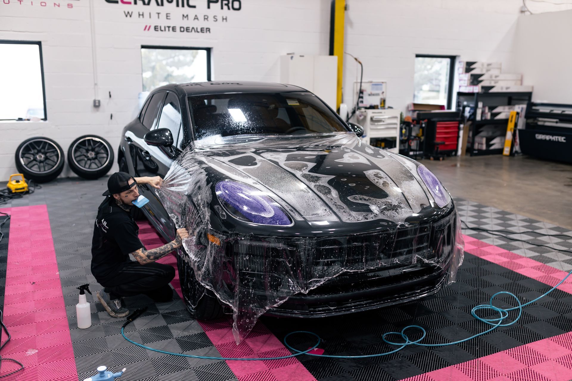 A man is wrapping a car with plastic wrap in a garage.