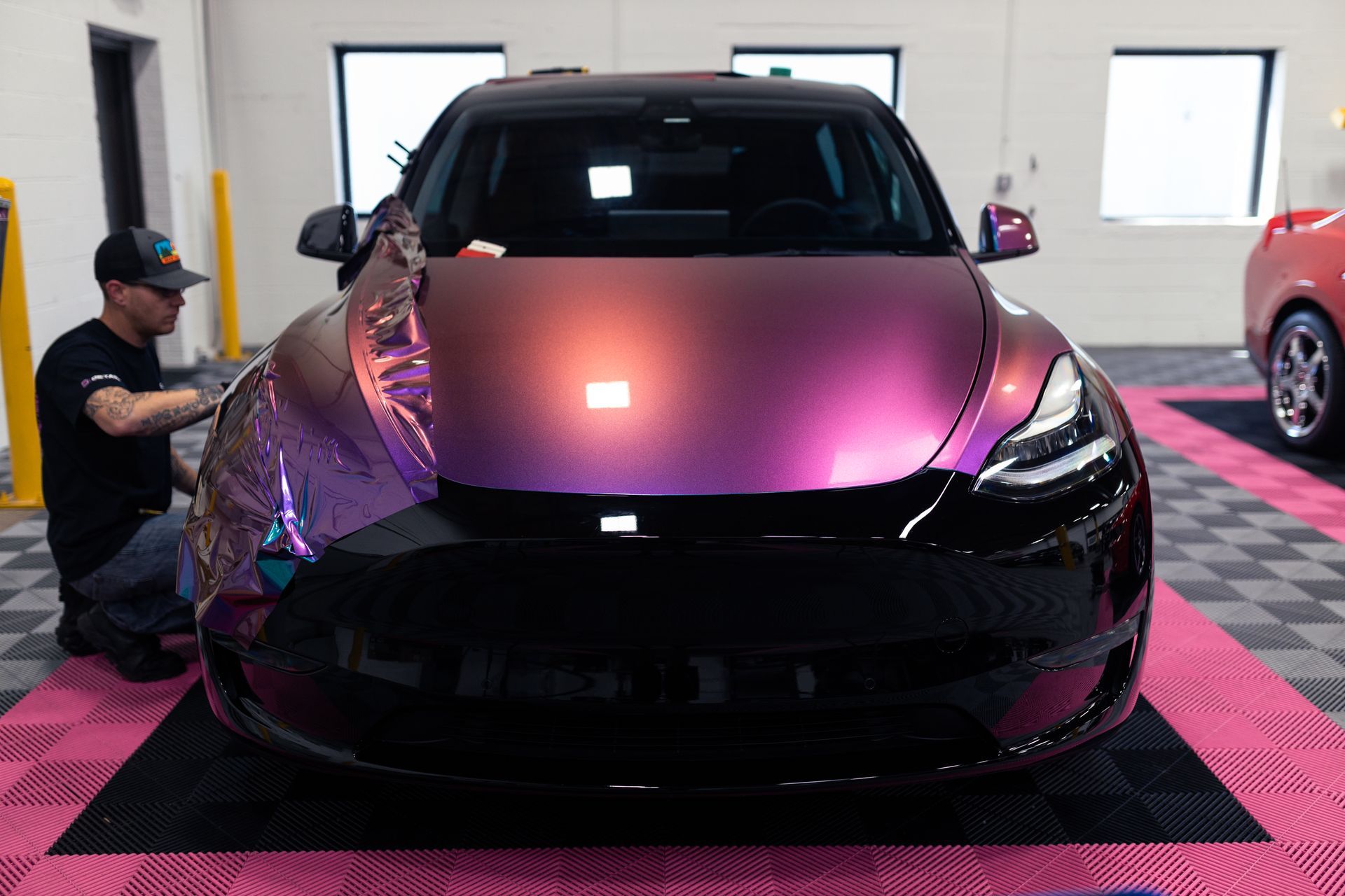 A man is working on a purple tesla model 3 in a garage.
