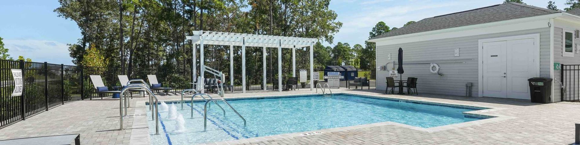 A swimming pool with white pergola, loungers, and a building on a sunny day.