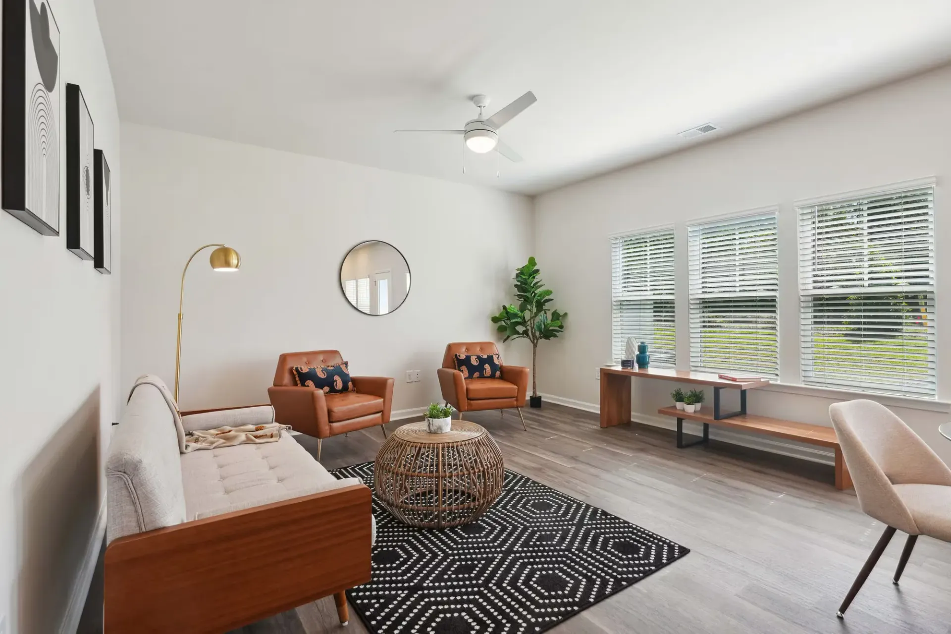 Bright loungewith beige sofa, two orange chairs, a round wicker coffee table, and a plant by the window.