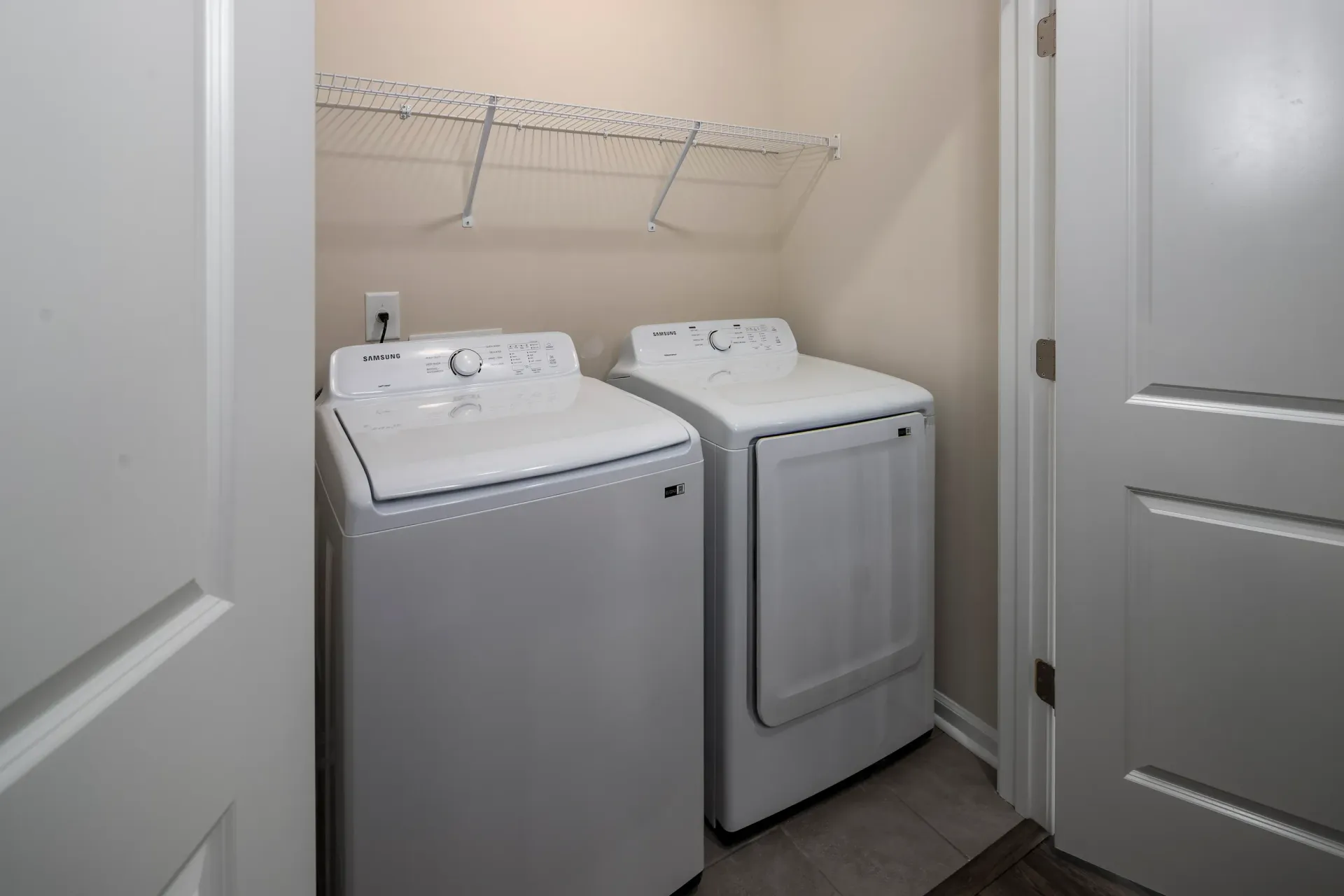 In-unit laundry closet with a side-by-side washer and front-load dryer and a wire shelf.