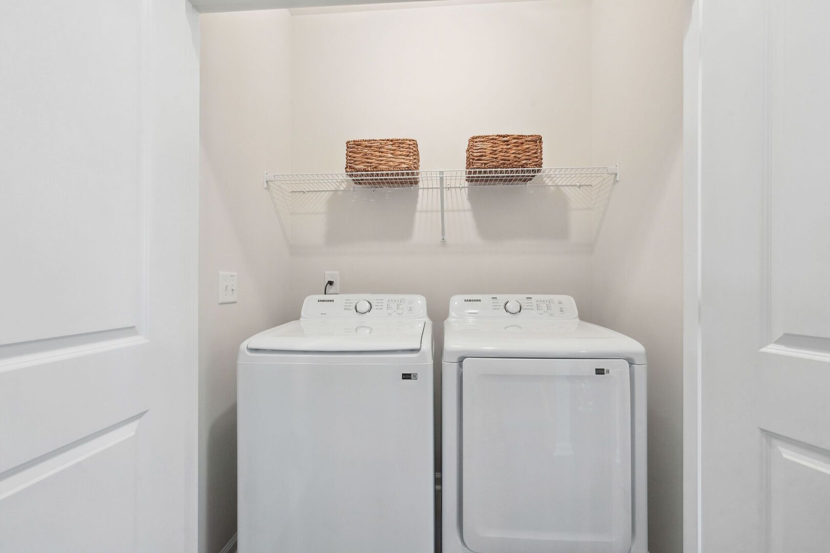 Laundry closet with a side-by-side washer and dryer under a wire shelf.