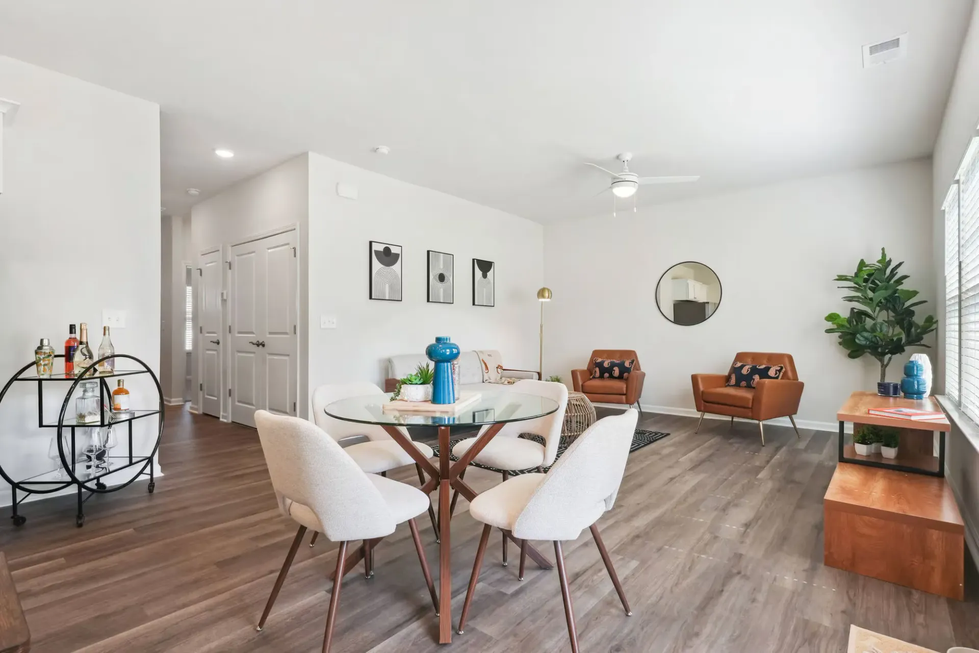 Bright open-plan living/dining room in a modern apartment with a round glass dining table and beige chairs.