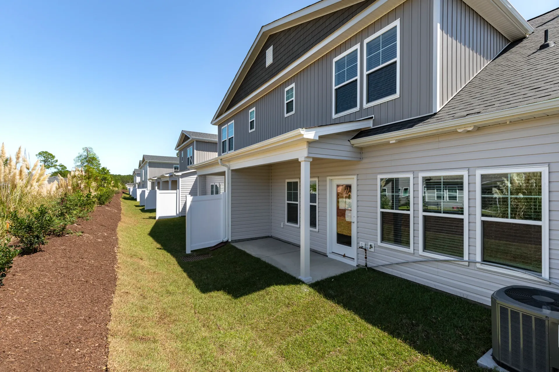 Exterior view of townhouse-style apartments with back patios, white fences, and green lawn.