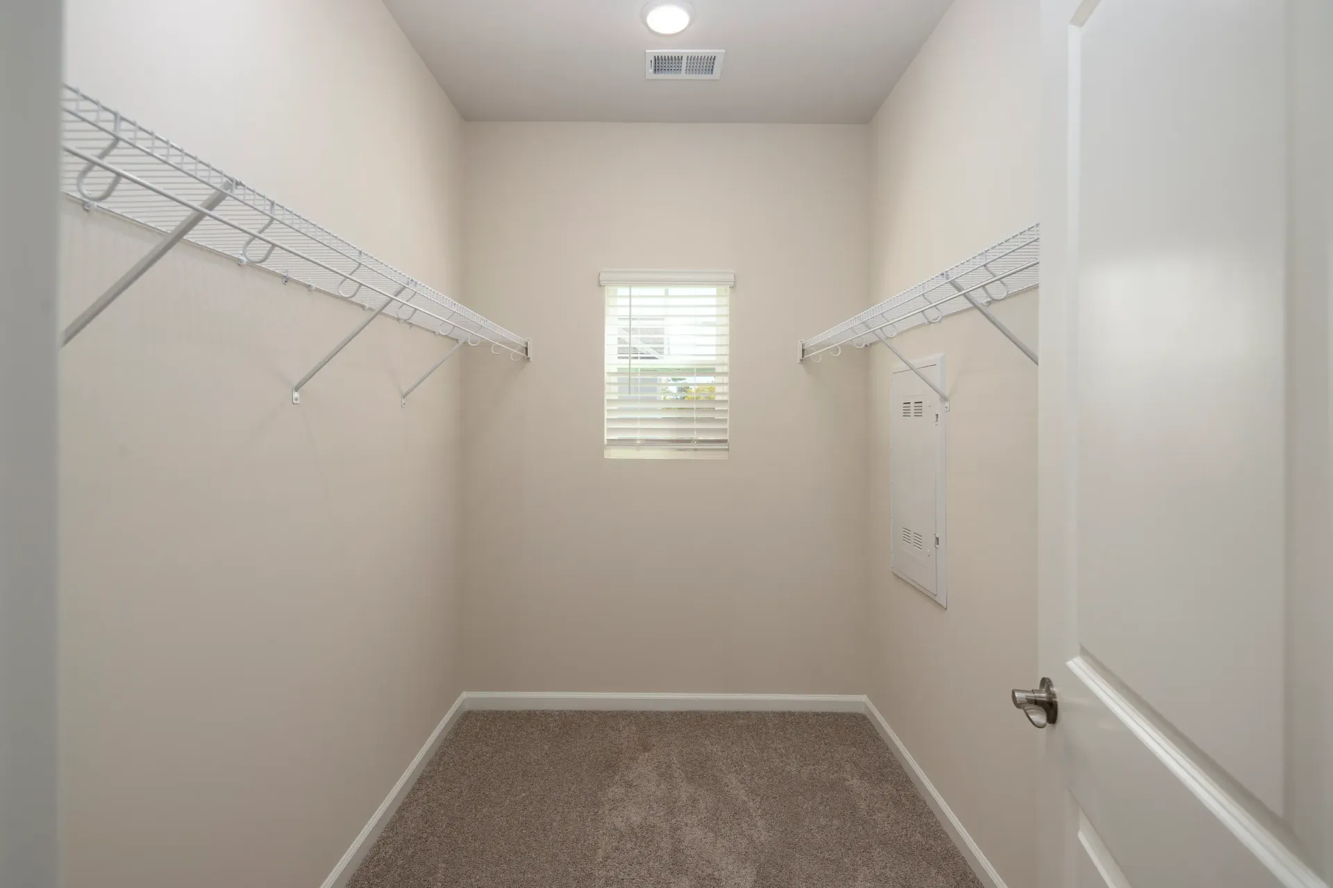 Walk-in closet with white wire shelving along both walls and a small window.