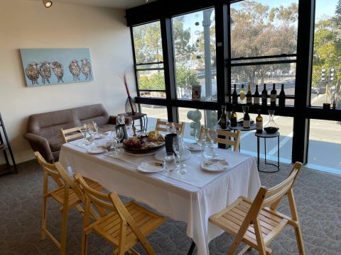 A table with a white tablecloth and wooden chairs in a room with a lot of windows.