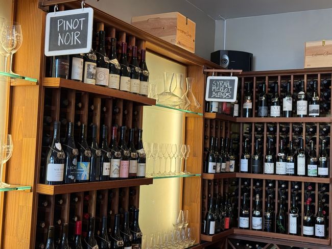 A shelf full of wine bottles with a sign that says pinot noir