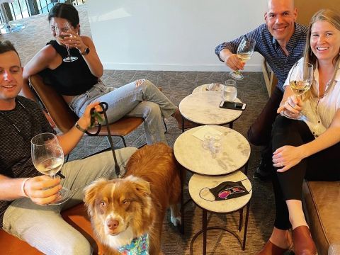 A group of people and a dog are sitting at a table drinking wine.