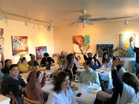 A group of people are sitting at tables with their hands in the air.