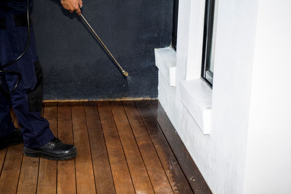 A Man Is Spraying A Wooden Floor With A Sprayer — ASAP Pest Control in Booval, QLD