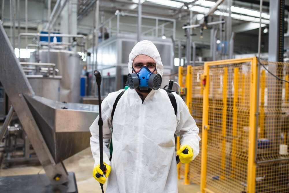 A Man In A Protective Suit And Mask Is Spraying Chemicals In A Factory — ASAP Pest Control in Rathdowney, QLD