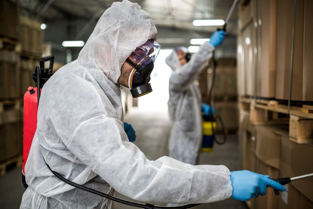 A Man In A Protective Suit Is Spraying A Warehouse With A Sprayer — ASAP Pest Control in Elanora, QLD