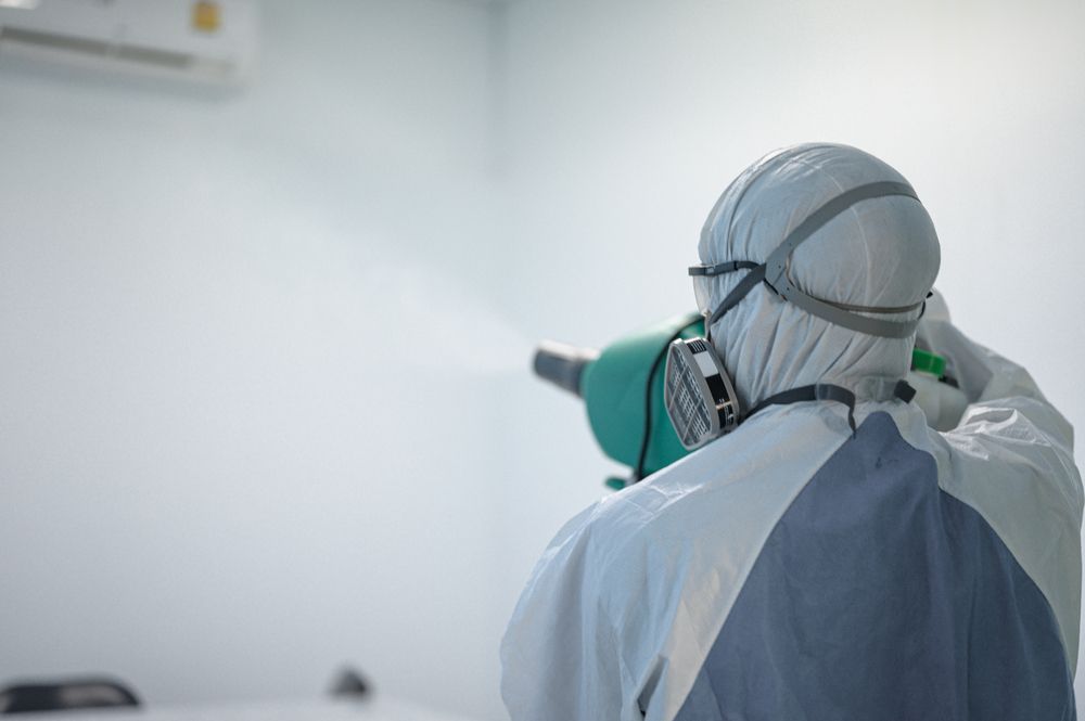 A Man In A Protective Suit Is Spraying A Room With A Sprayer — ASAP Pest Control in Brisbane South, QLD