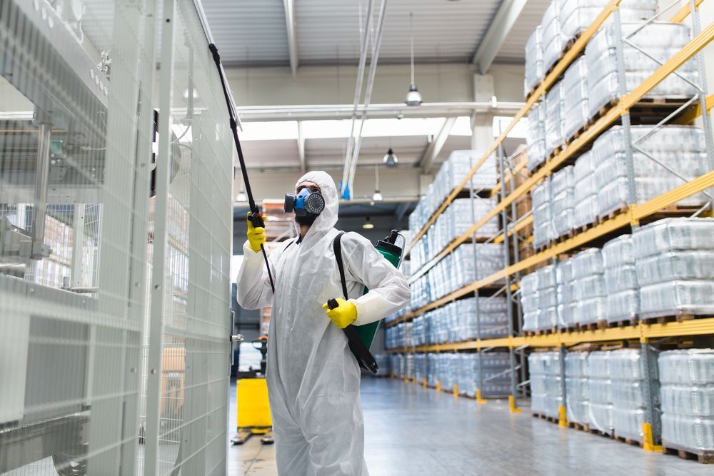 A Man In A Protective Suit Is Spraying A Warehouse With A Sprayer — ASAP Pest Control in Broadbeach, QLD