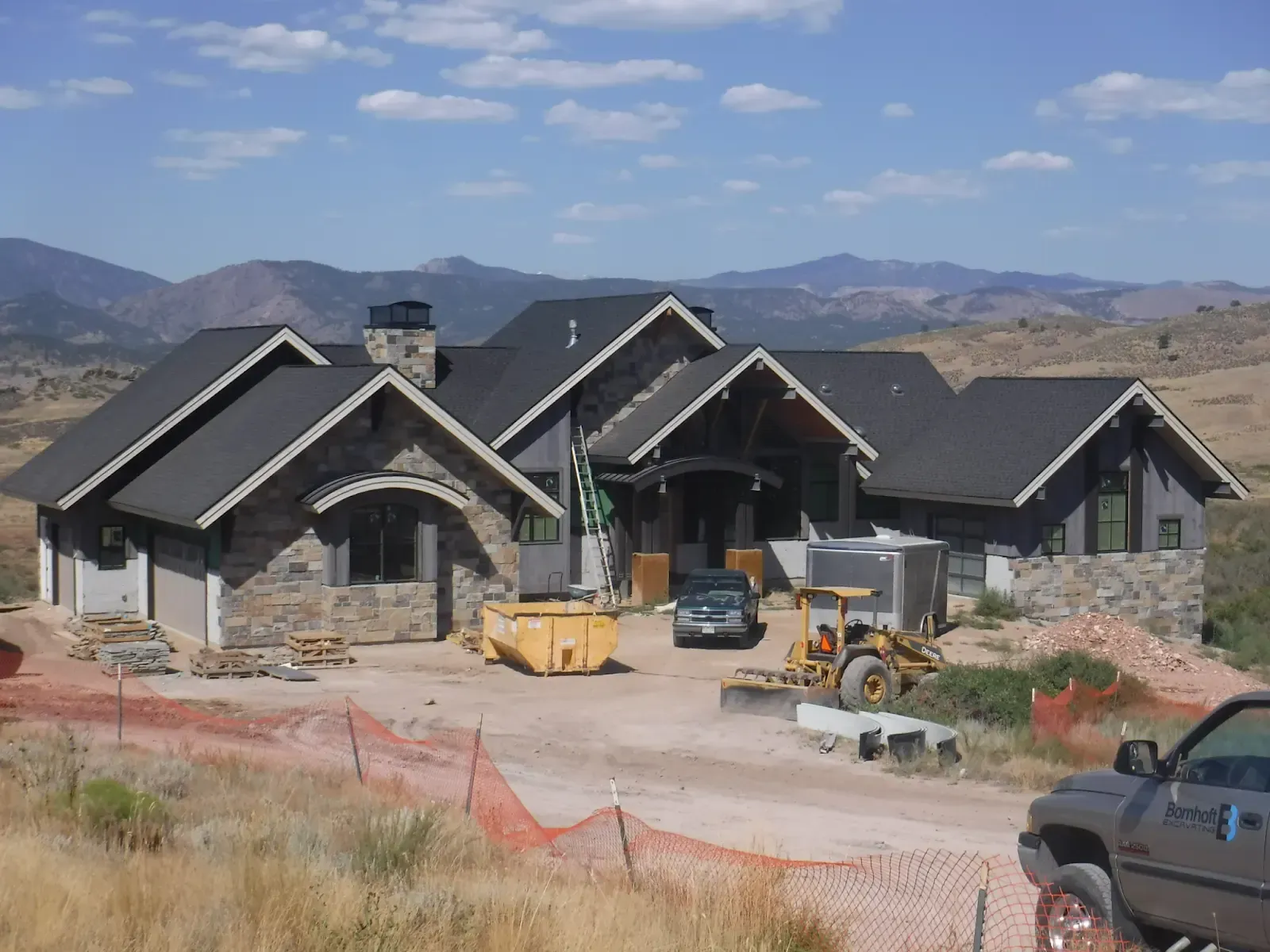 House under construction with stone and gray siding, black roof, and mountain backdrop.