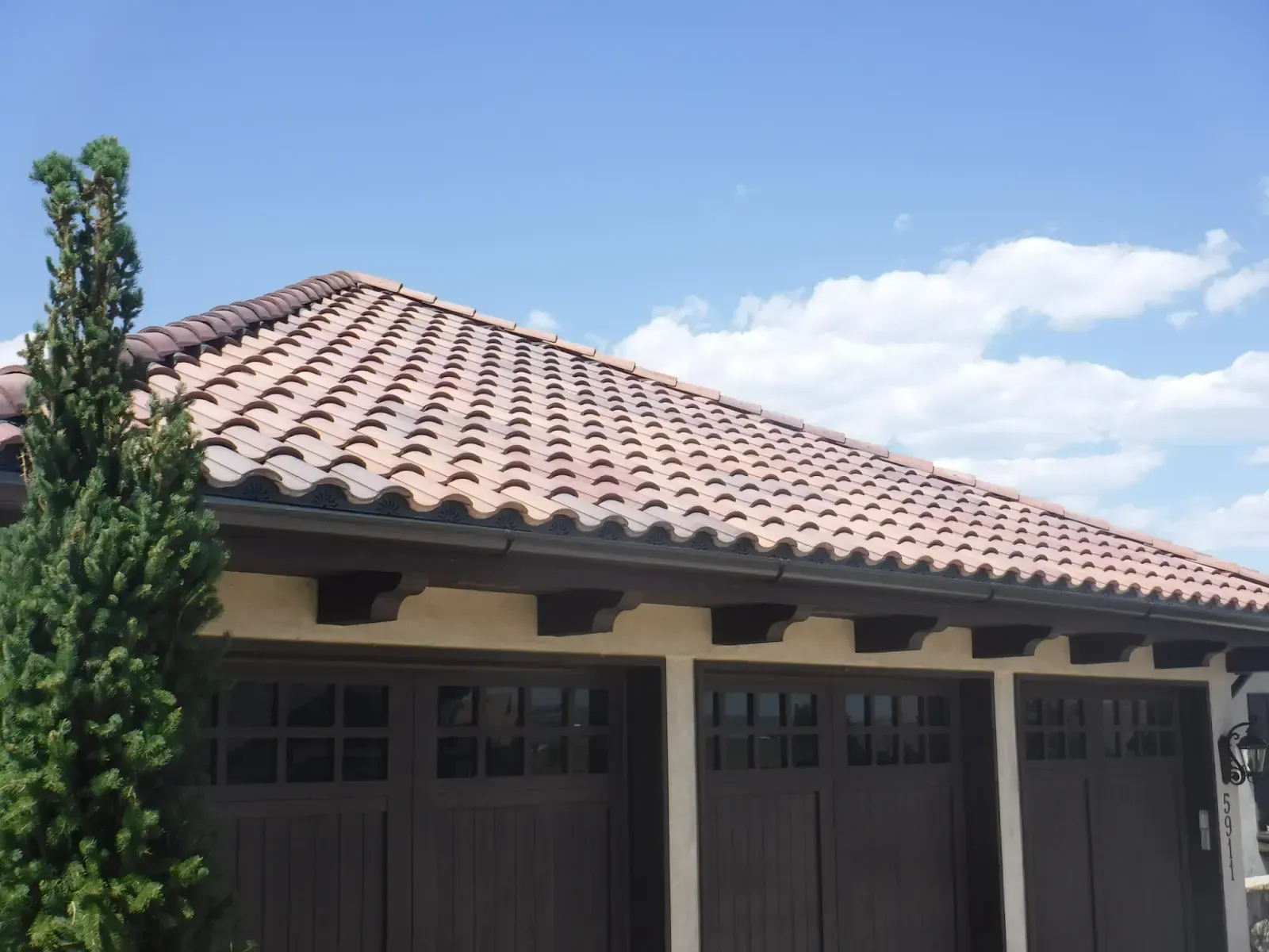 Brown tile roof over a garage with three dark brown doors, against a bright blue sky.