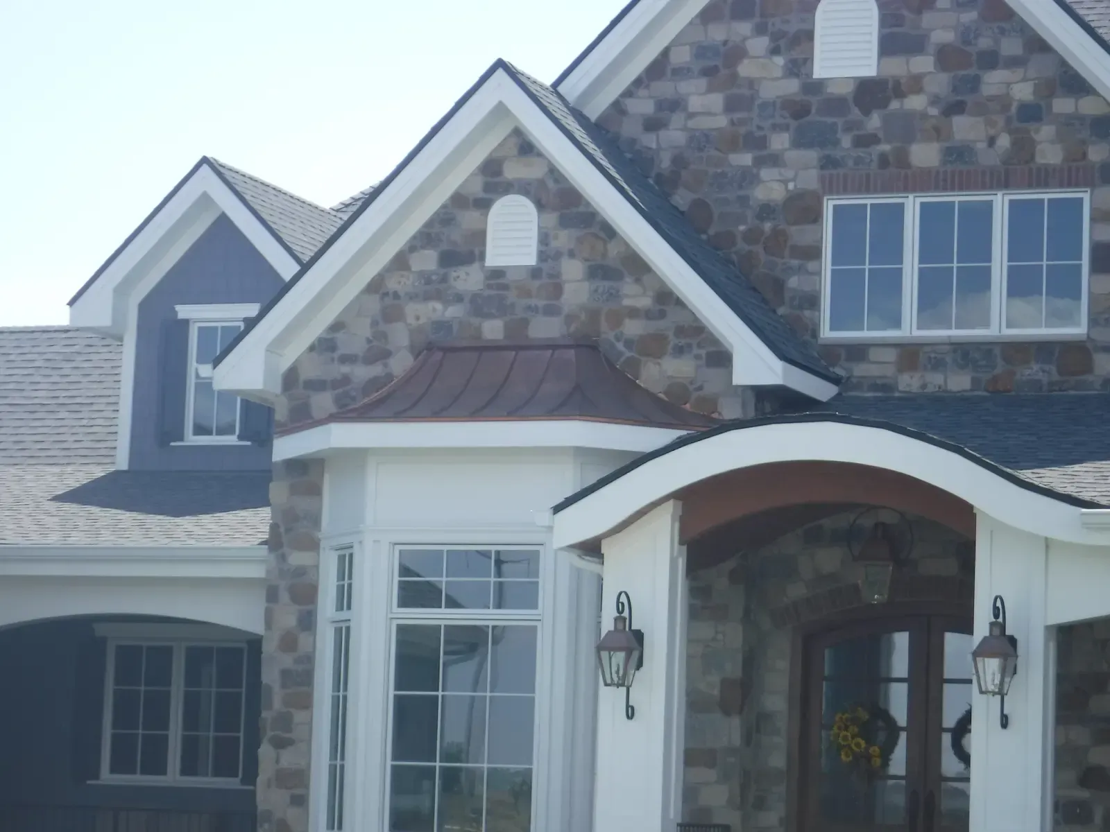 Stone and blue siding home with white trim and copper awning.
