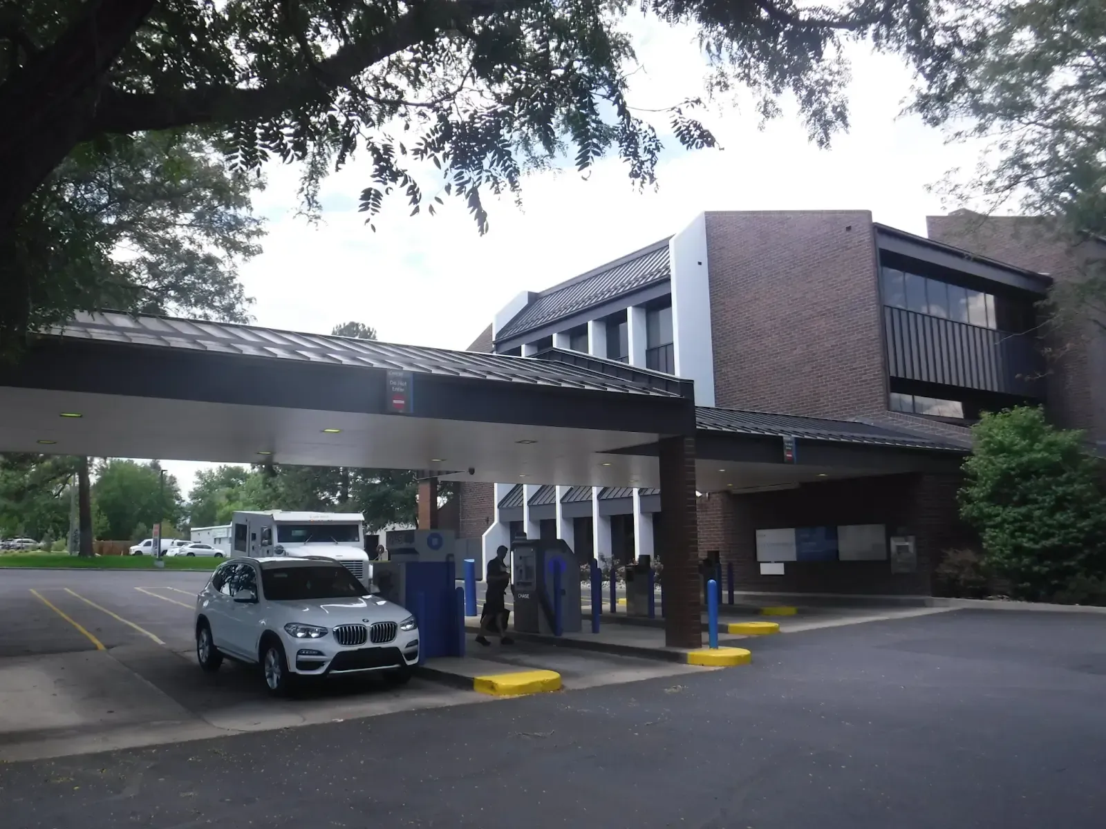 Exterior of a building with a covered drive-up area; a white SUV is parked there.