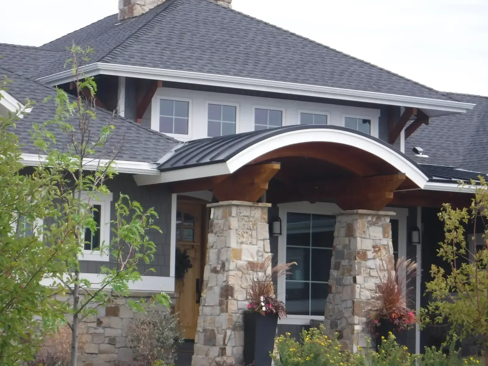 Dark gray house with stone pillars, a curved wooden entryway, and a dark roof.