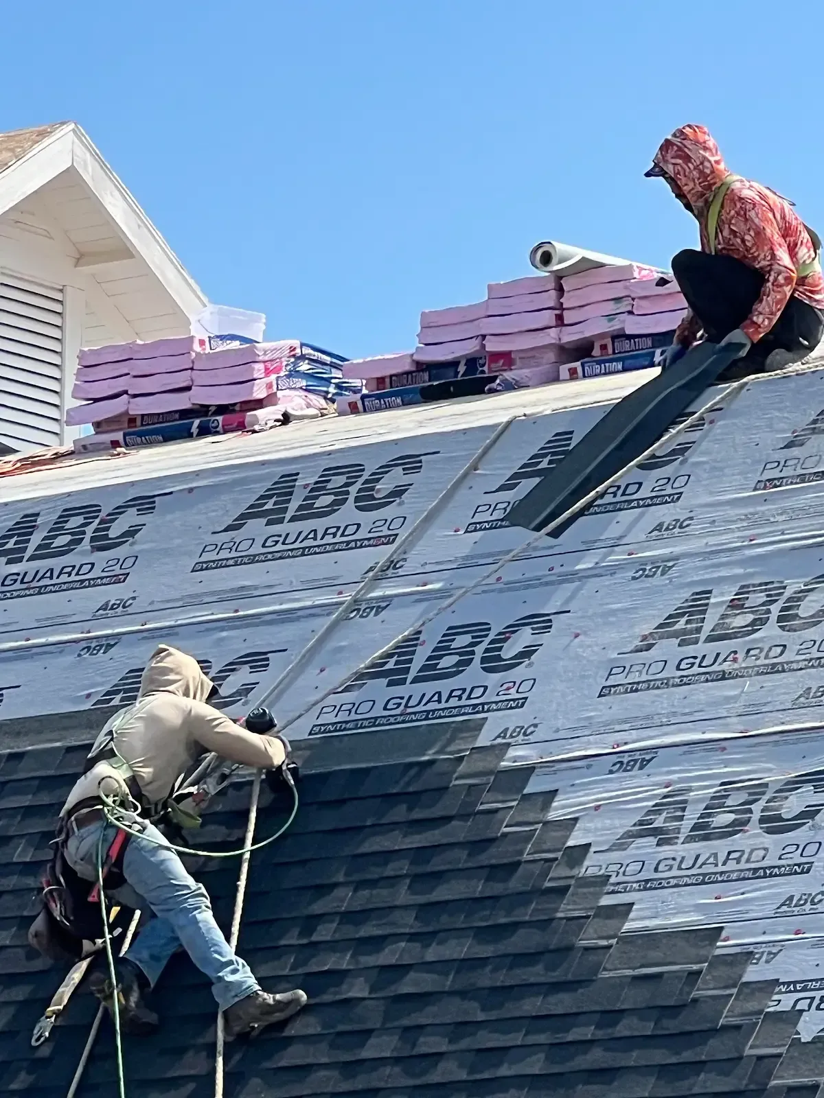 Two roofers installing shingles on a house roof on a sunny day.