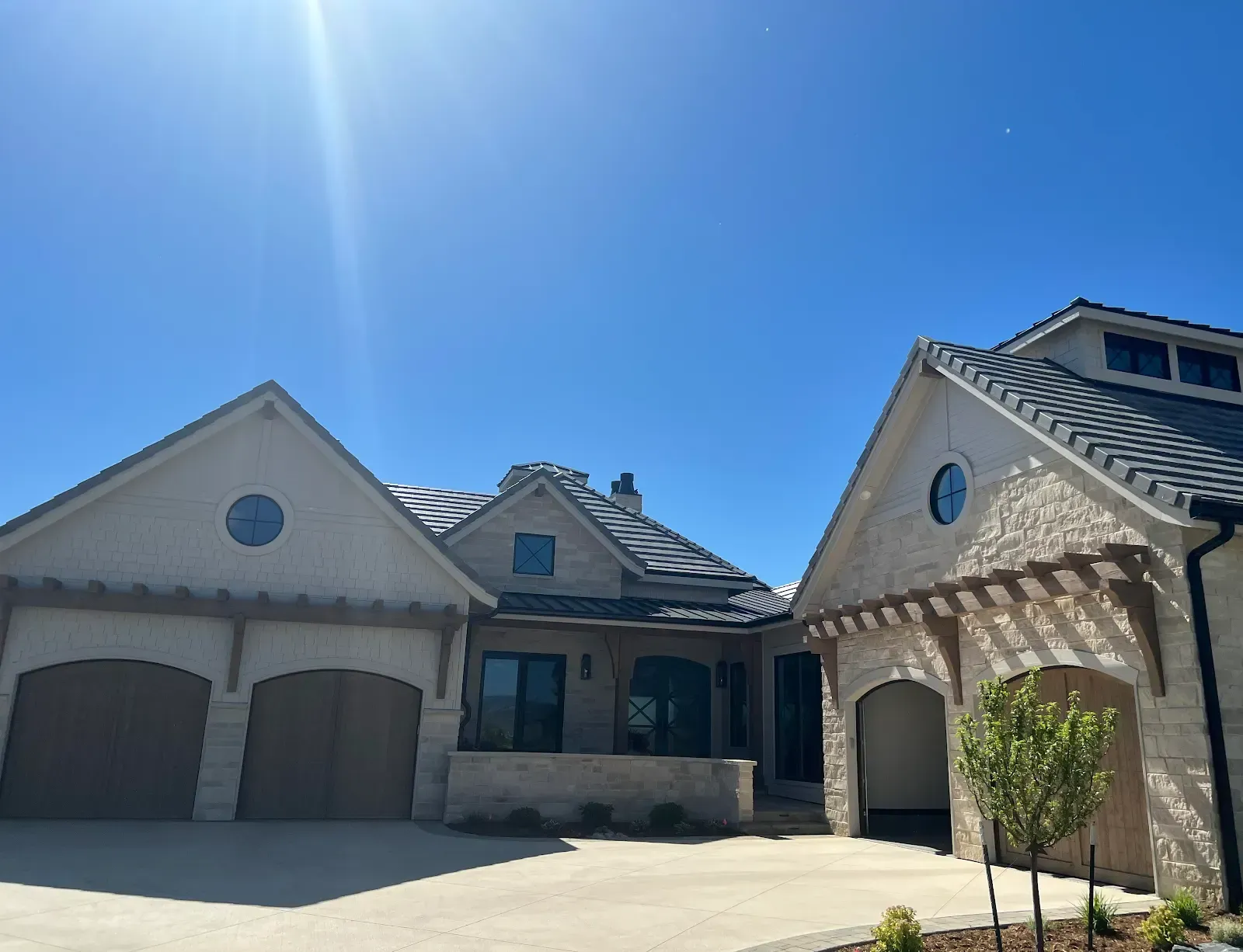 Beige stone house with dark gray roof, two car garage, and a sunny blue sky.