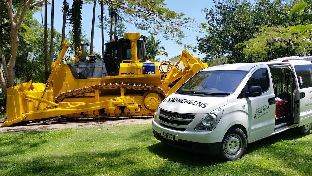 A White Van is Parked Next to a Large Yellow Bulldozer — Sunshine Coast Windscreens In Maroochydore, QLD