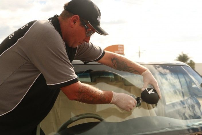 A Man is Fixing a Windshield on a Car — Sunshine Coast Windscreens In Buderim, QLD