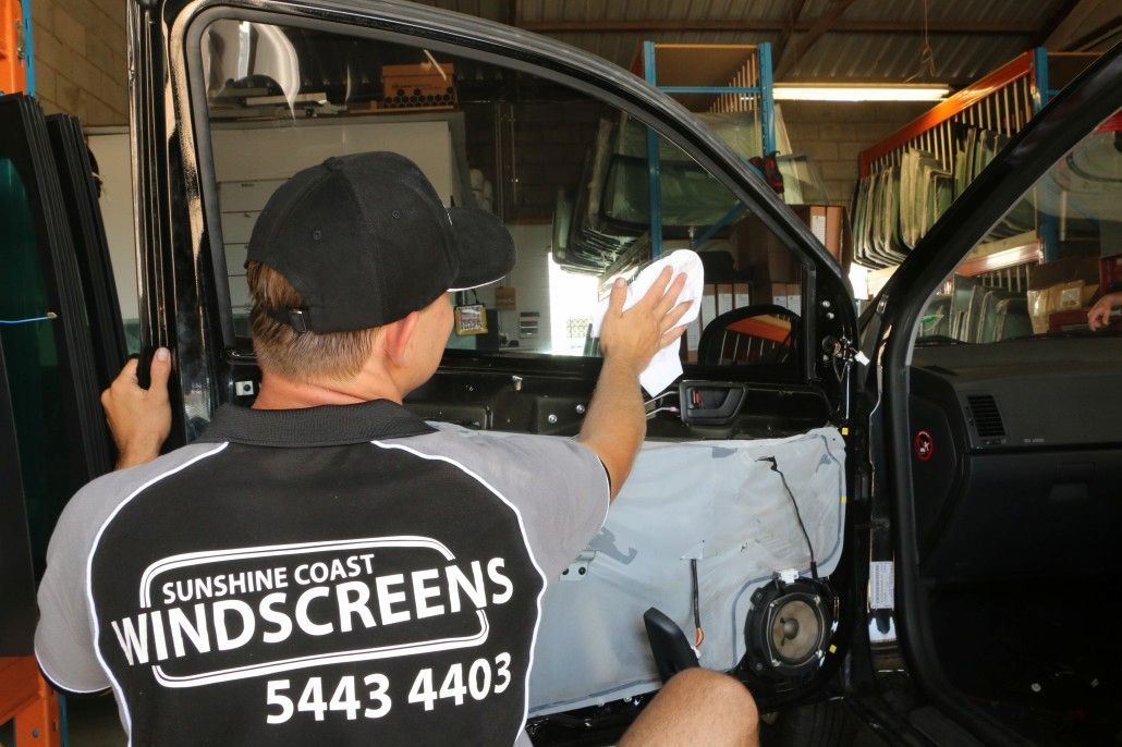 A Man Wearing a Sunshine Coast Windscreens Shirt is Working on a Car — Sunshine Coast Windscreens In Buderim, QLD