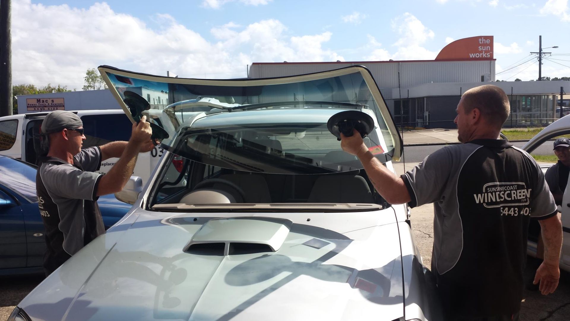 Two Men Removing a Windshield From a Silver Car Outdoors, Under a Blue Sky — Sunshine Coast Windscreens In Buderim, QLD