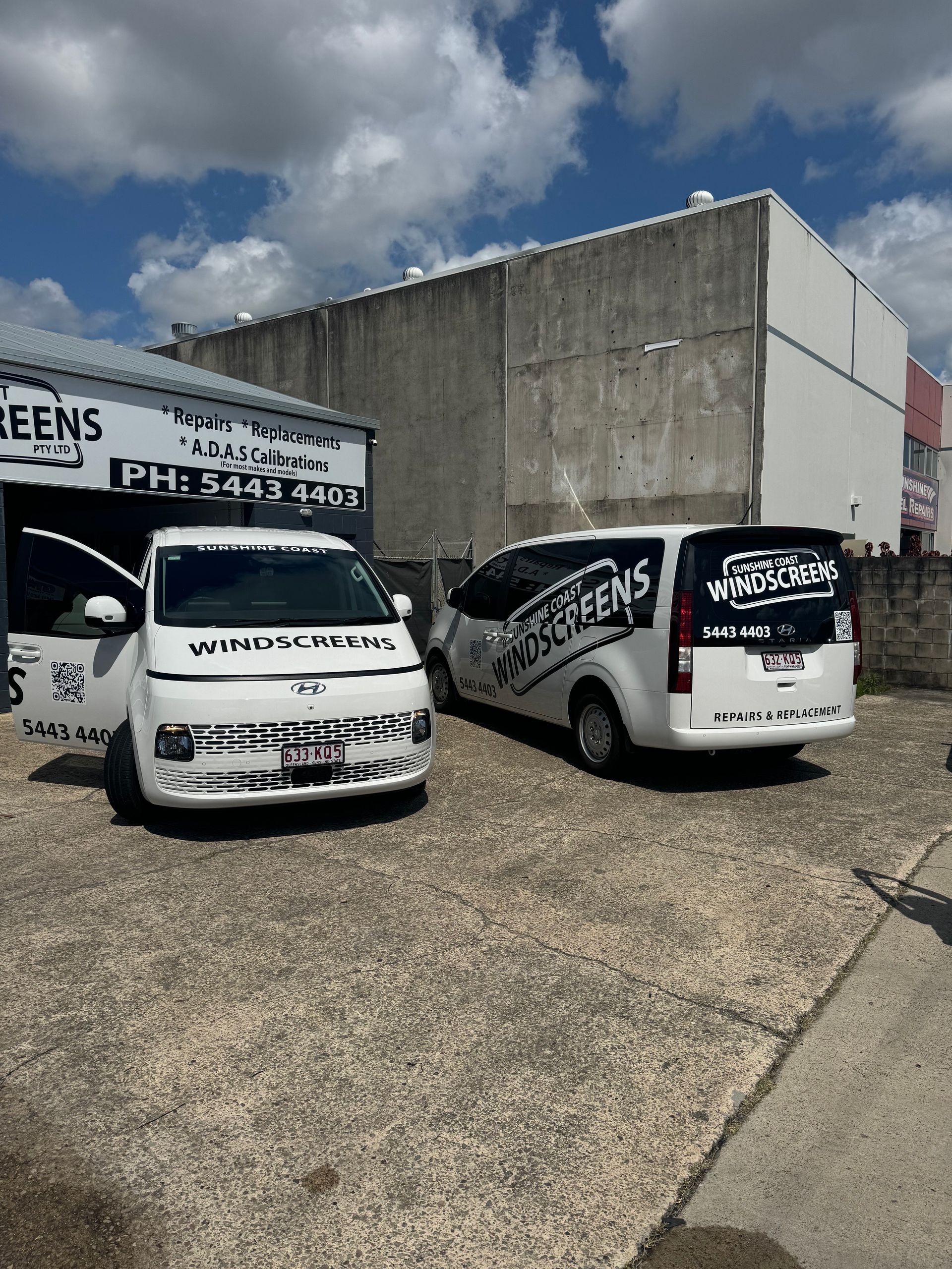 Two white vans are parked in front of a building.