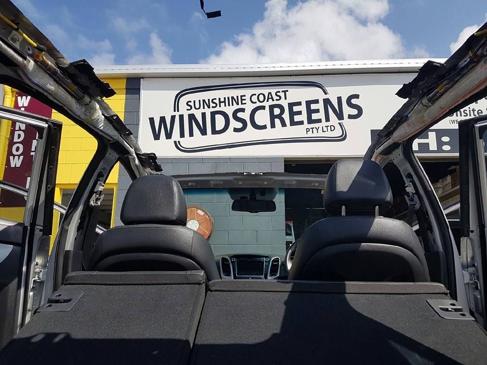 A car is parked in front of a sign that says sunshine coast windscreens