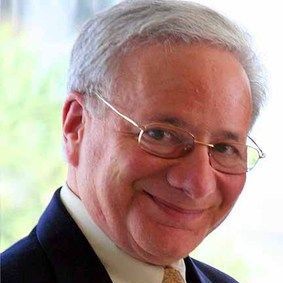 david brams A man wearing glasses and a suit is smiling for the camera.