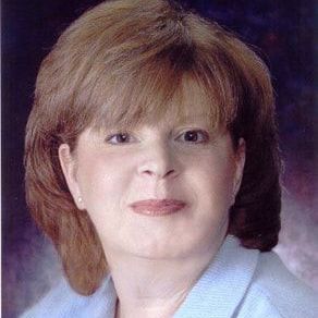 A woman with red hair is wearing a blue shirt and smiling for the camera.